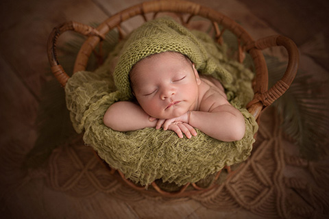 Bebé dormido con gorro verde dentro de una cesta.