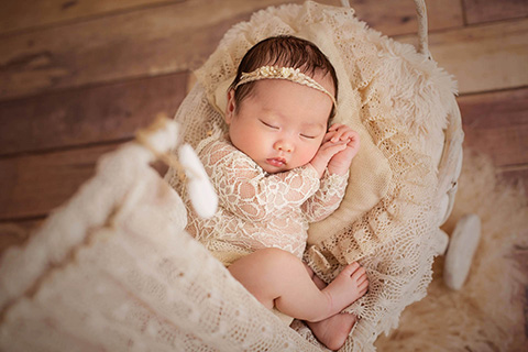 Bebé china dormida en una cuna en color beige, tiene las manos entrelazadas y las piernas flexionadas.