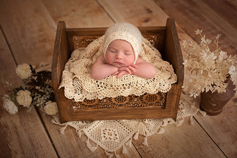 Lindo bebé duerme sobre un cajón de madera, con gorro de lana y encaje apoya su cabecita sobre una manta de ganchillo.